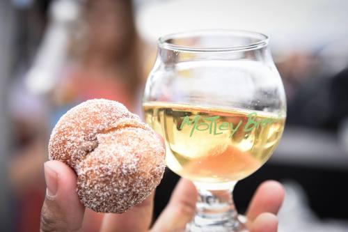 A hand holding a sugared donut and a glass of light-colored beverage with a logo.
