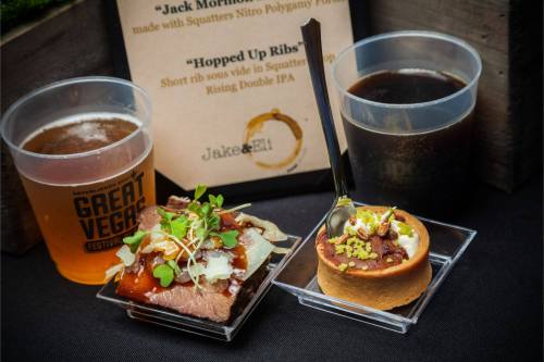 A plate with brisket topped with sauce and microgreens, a dessert tart, and two cups of beer on a table.