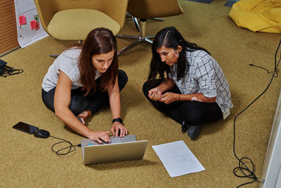 Dois funcionários sentados no chão do escritório da IBM trabalhando em um notebook