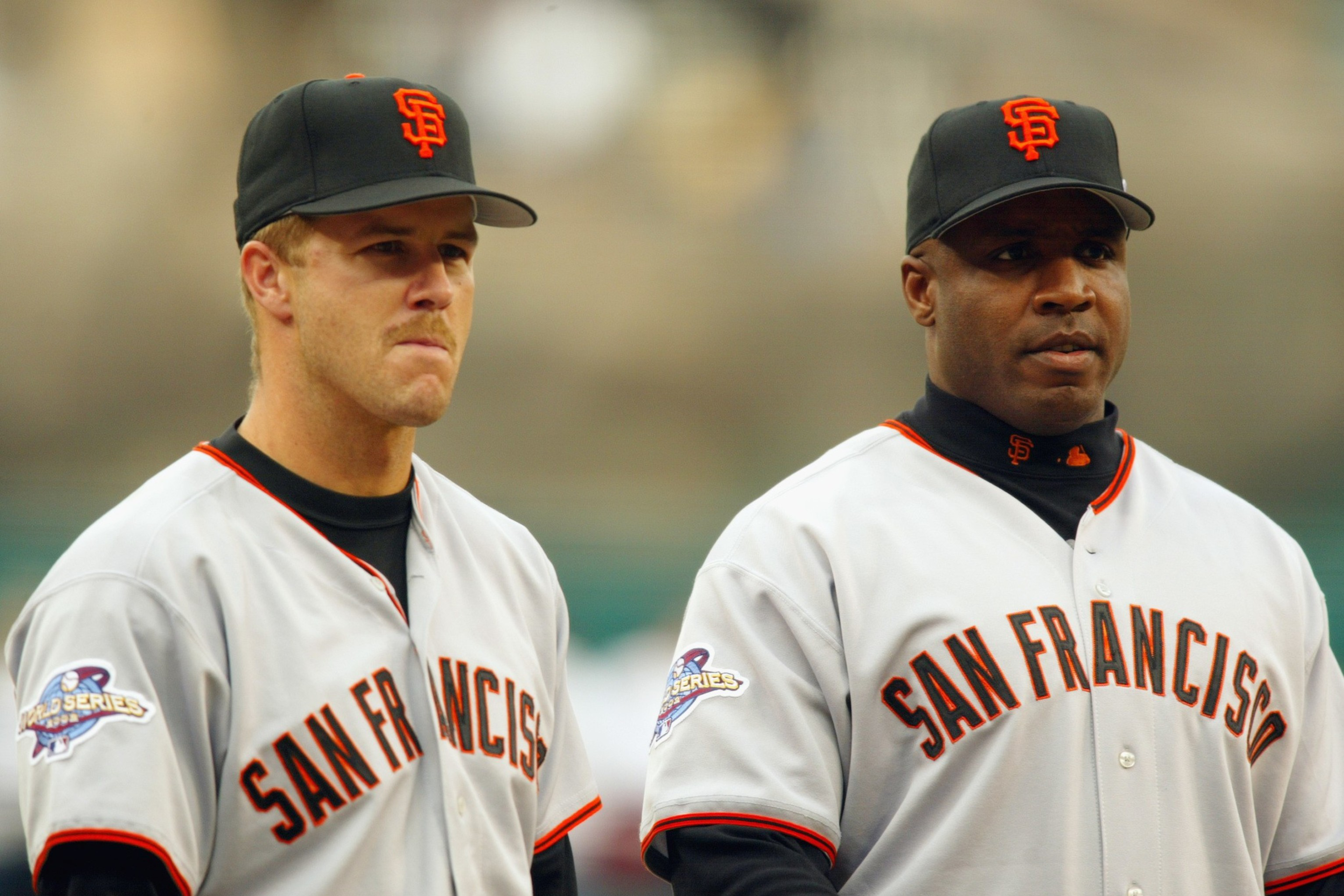 Two San Francisco Giants players in gray uniforms with black and orange caps stand side by side, both wearing World Series patches on their sleeves.