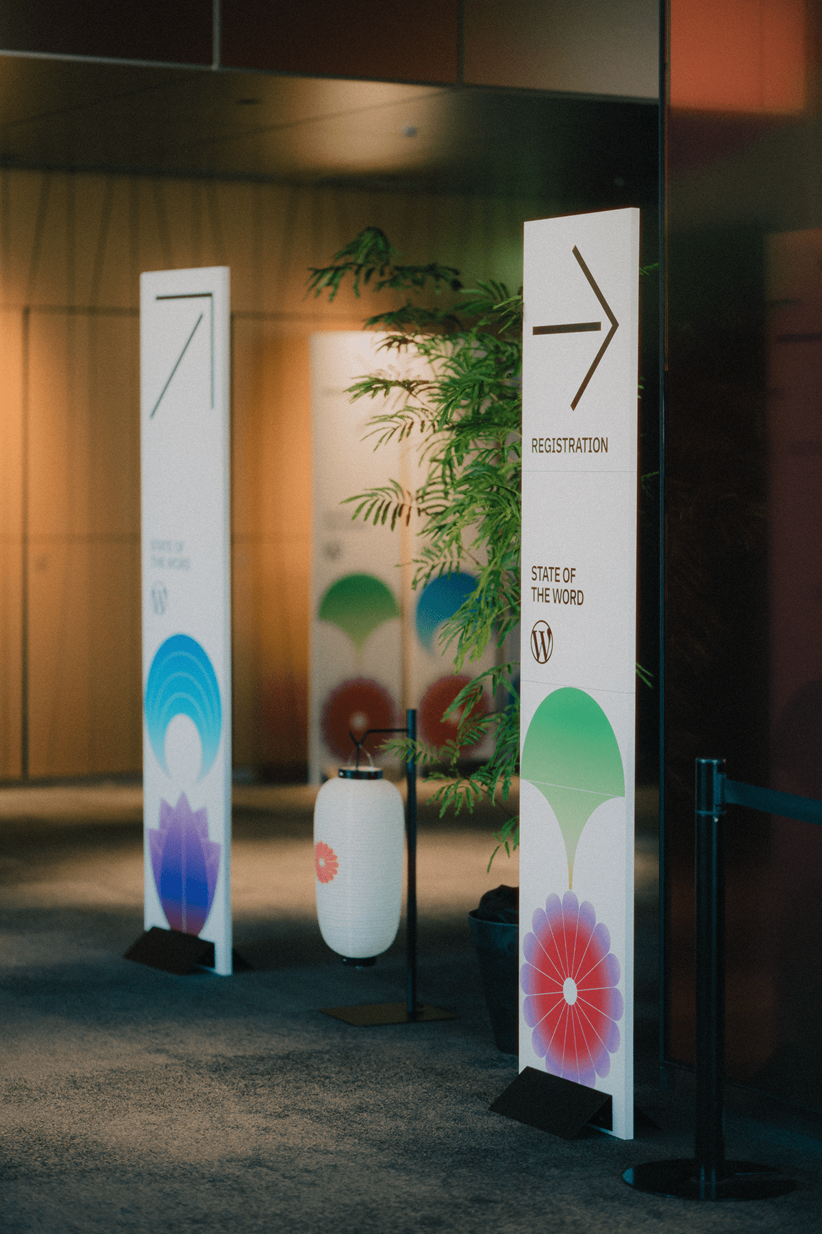Entrance area for an event featuring registration signage and decorative elements, including plants and lanterns.