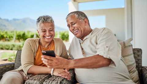 a couple on their porch laughing while looking at a smart phone