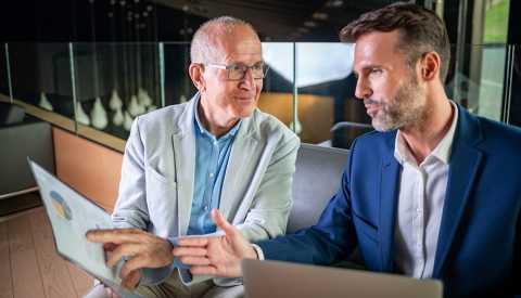 a younger businessman and an older one discuss a plan