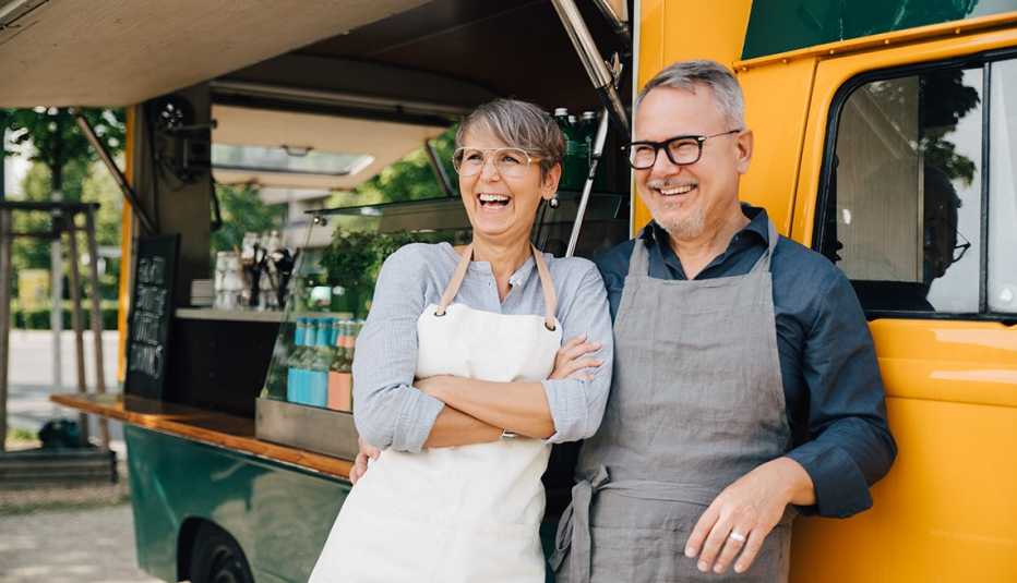 Pareja sonriendo y recostada sobre la puerta de su camión de comidas.