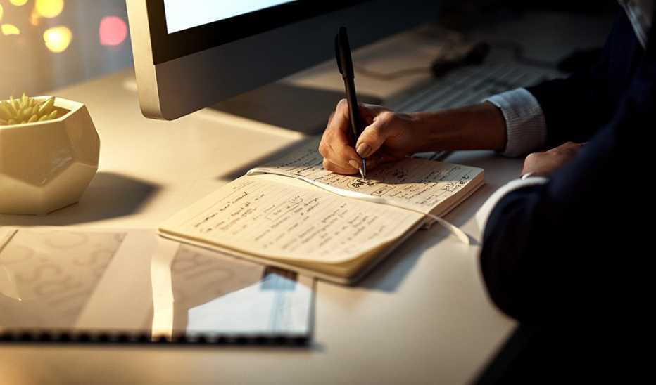 A hand writing notes at an office desk at night