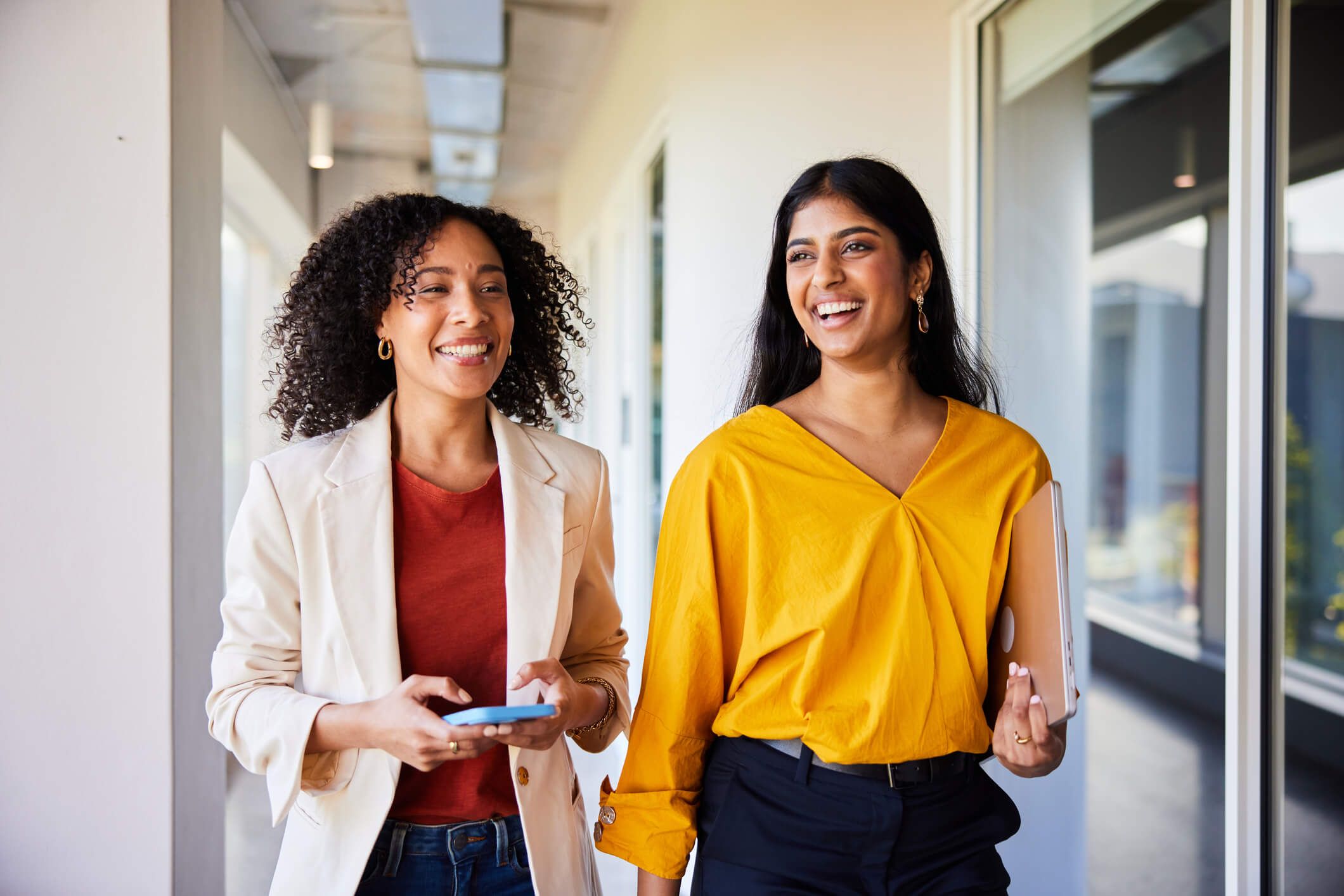 A man and woman walking together through a modern office building, engaged in conversation and surrounded by glass walls.