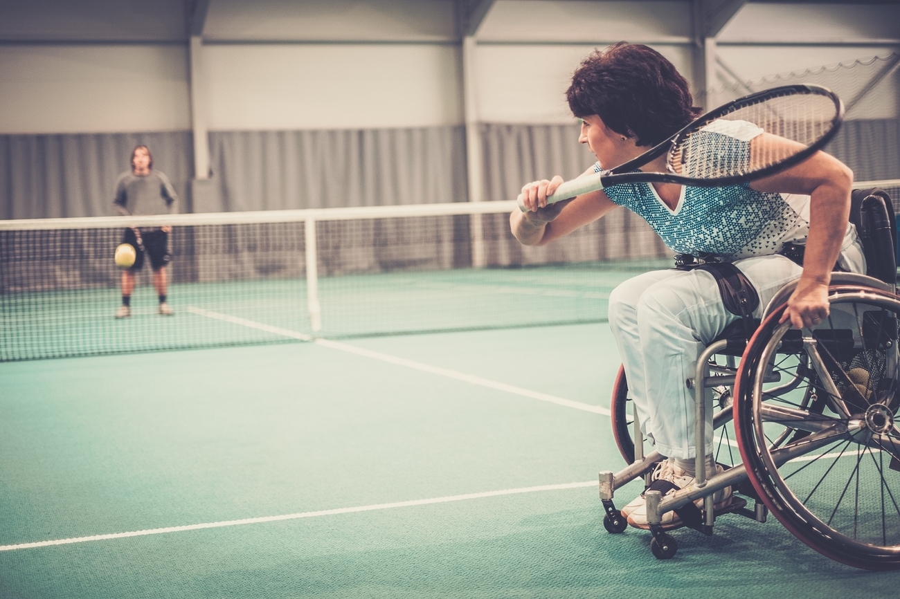A woman in a wheelchair playing tennis on a sunny day.