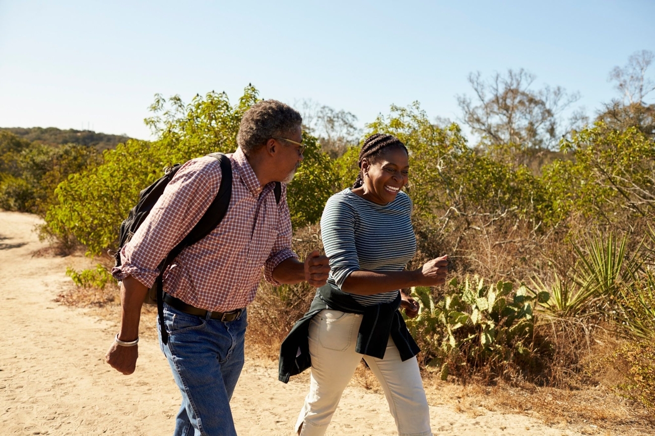 An elderly man and woman stroll along a dusty trail, holding hands and enjoying a leisurely walk.