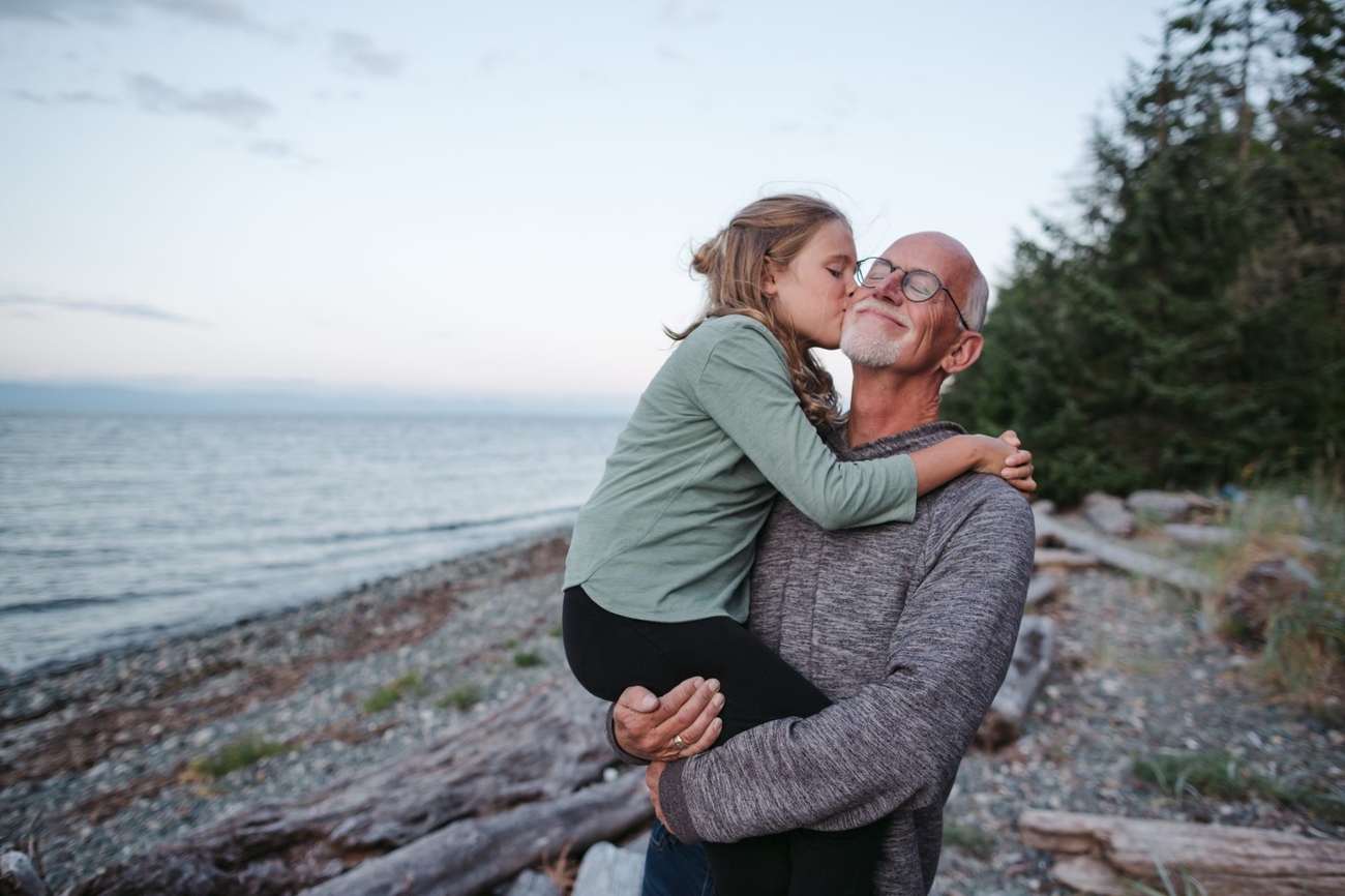 An older man and a little girl embracing on the sandy beach.