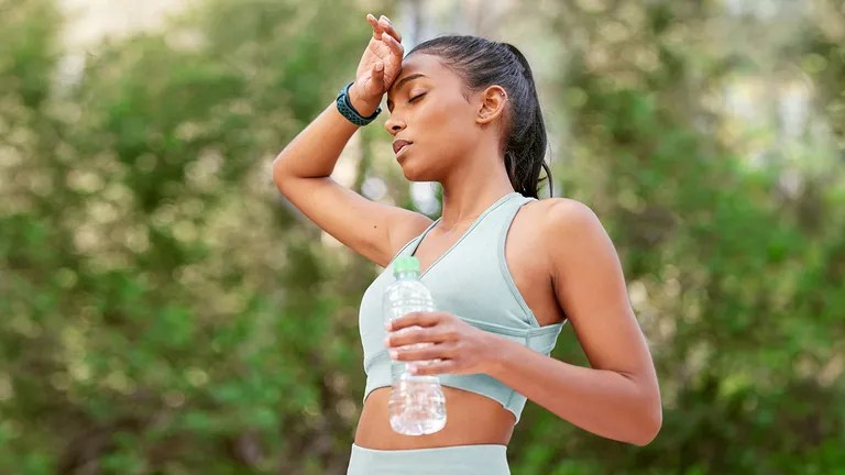 girl working out outside and putting her had against her head and holding a water bottle