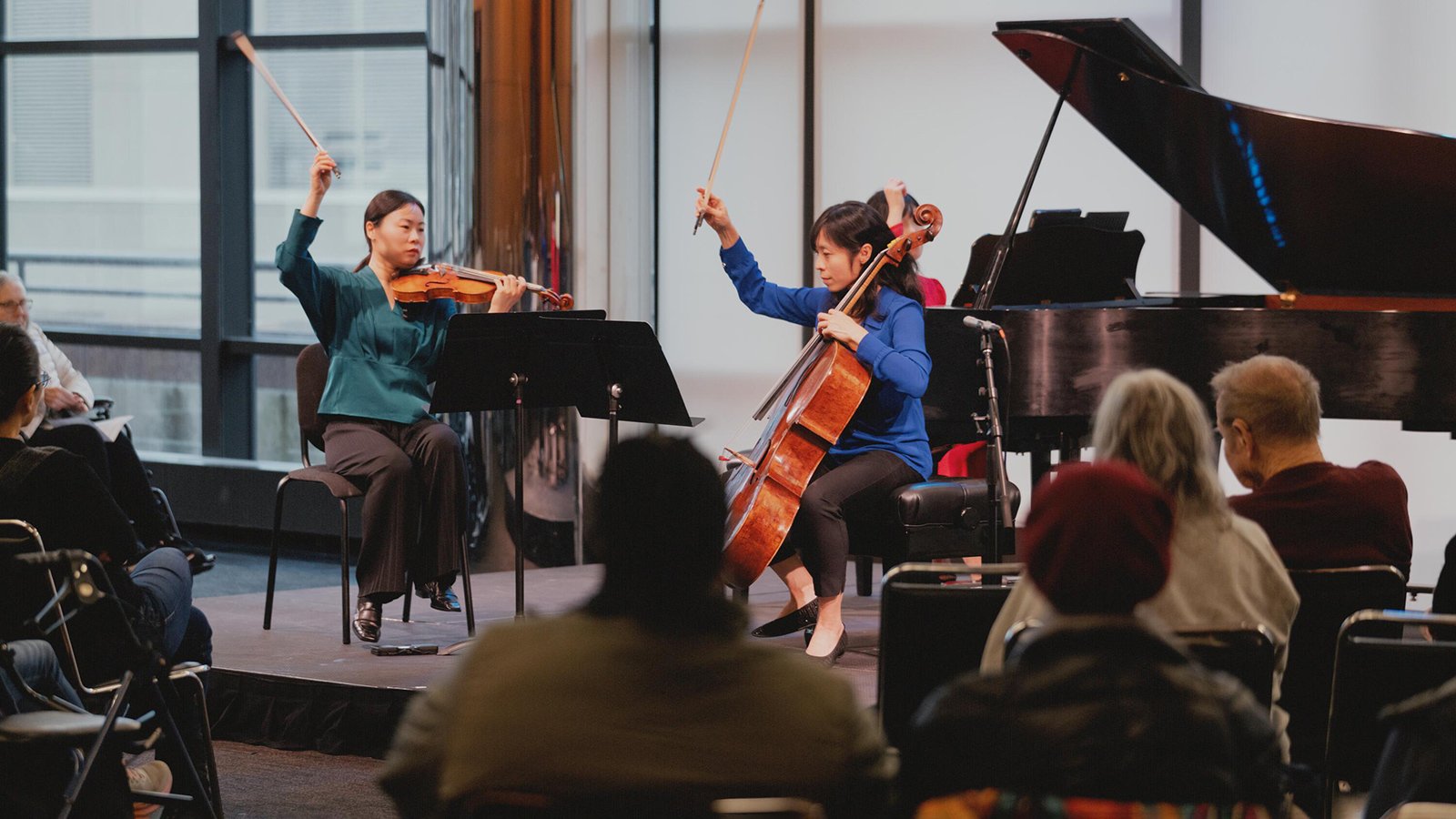An audience watches a violinist, cellist and pianist perform onstage at the Kaplan Penthouse.