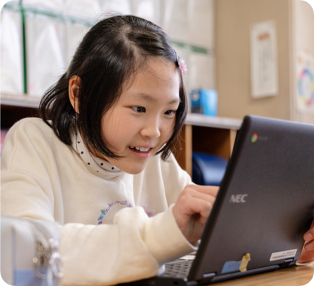 教室でタッチスクリーン付き Chromebook デバイスを使用している笑顔の児童。