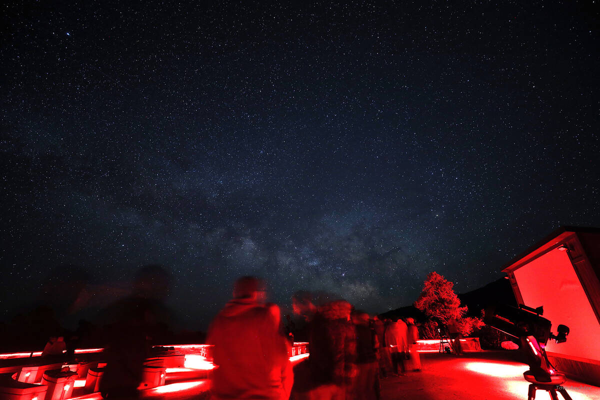 Red lit amphitheater with a colorful Milky Way over visitors waiting in line to view stars. (Gr ...
