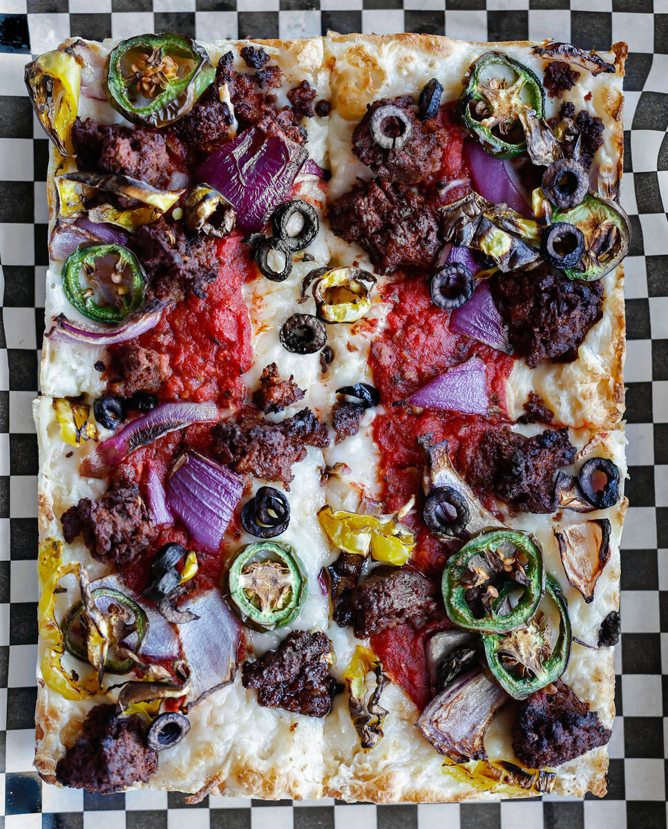 A vegan pizza with vegan cheese, vegan sausage, jalapeño, red onion and black olive is see ...