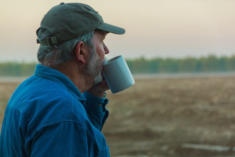 Senior male farmer contemplating field with coffee in morning