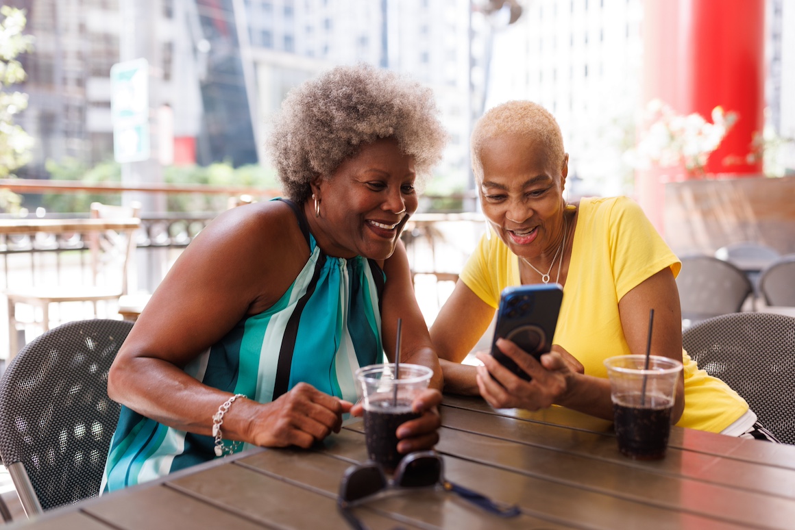 Smiling senior Black female friends surfing the internet and having fun at a cafe