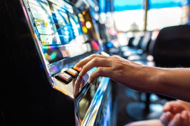 Focus is on a hand playing a slot machine at a casino.