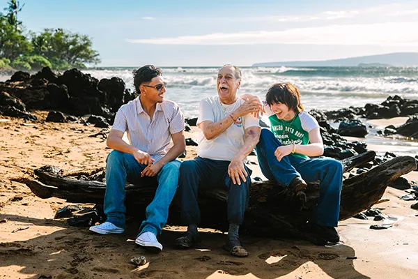 PPIR-Colorado-NASCAR-Wish-Lifetime-AARP-raceday An older man and two younger men laugh while sitting on the beach.