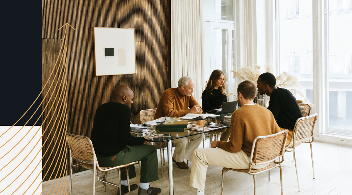 Five diverse coworkers in a modern, minimalist office space collaborating around a glass meeting table. The group, dressed in neutral and earthy tones, reviews documents and laptops in a bright room with floor-to-ceiling windows and a textured wood accent wall.