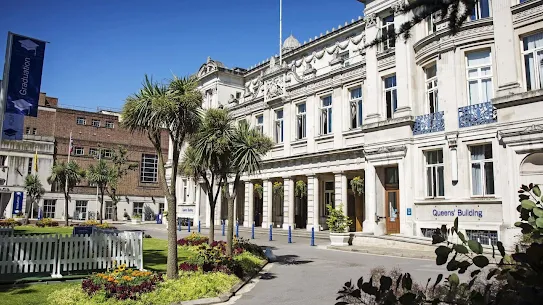 A grand, light-colored building with multiple windows and columns stands under a clear blue sky, flanked by palm trees and gardens.
